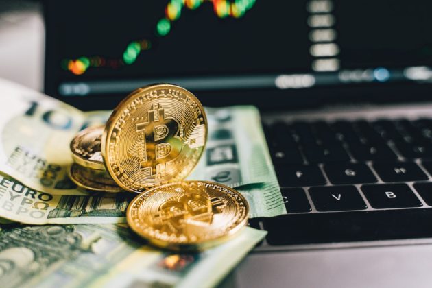 Physical bitcoin coin on top of dollar bills next to an open laptop.