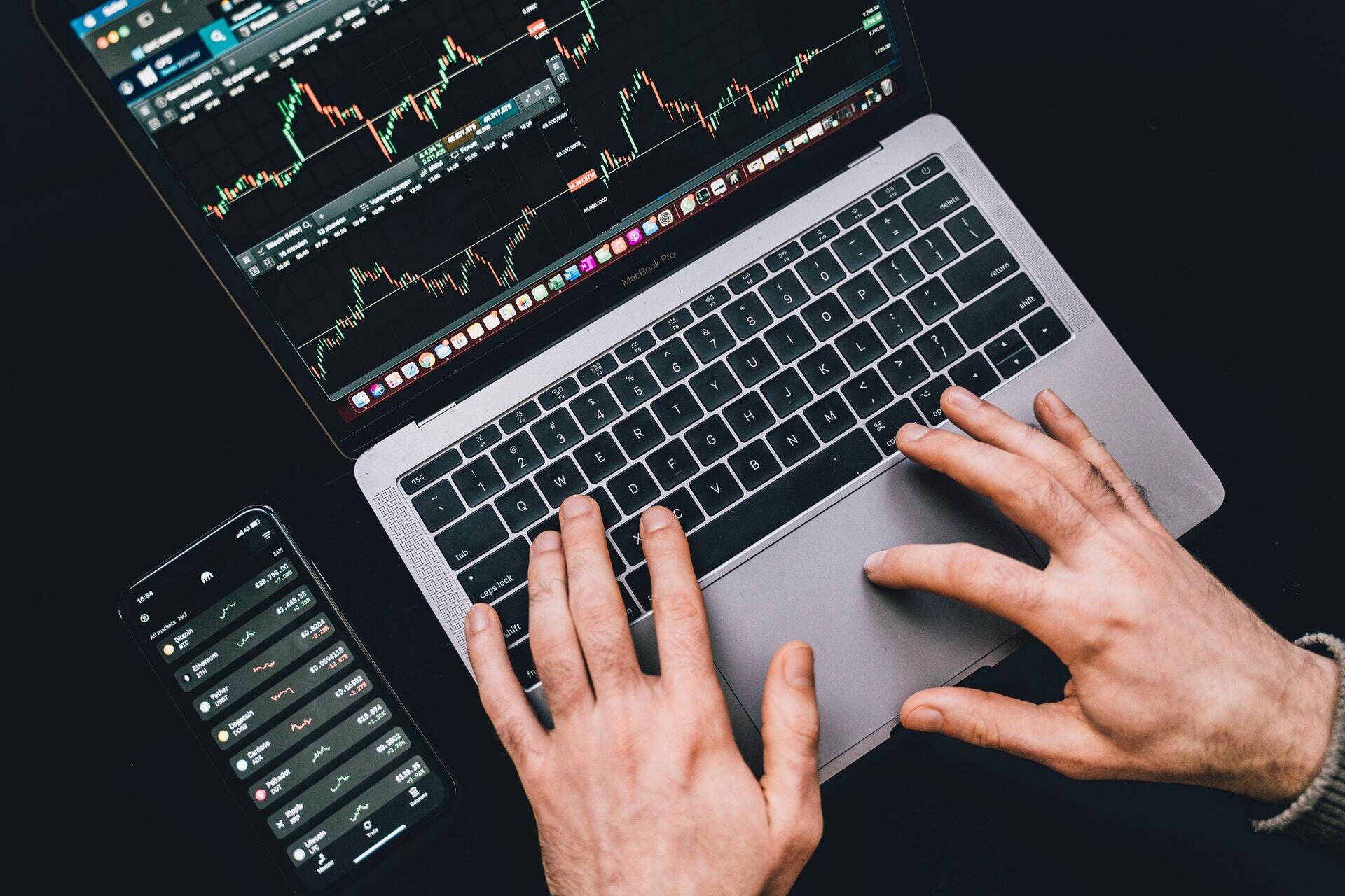 Overhead photo of someone typing on a macbook with a candlestick chart displayed on the screen. 