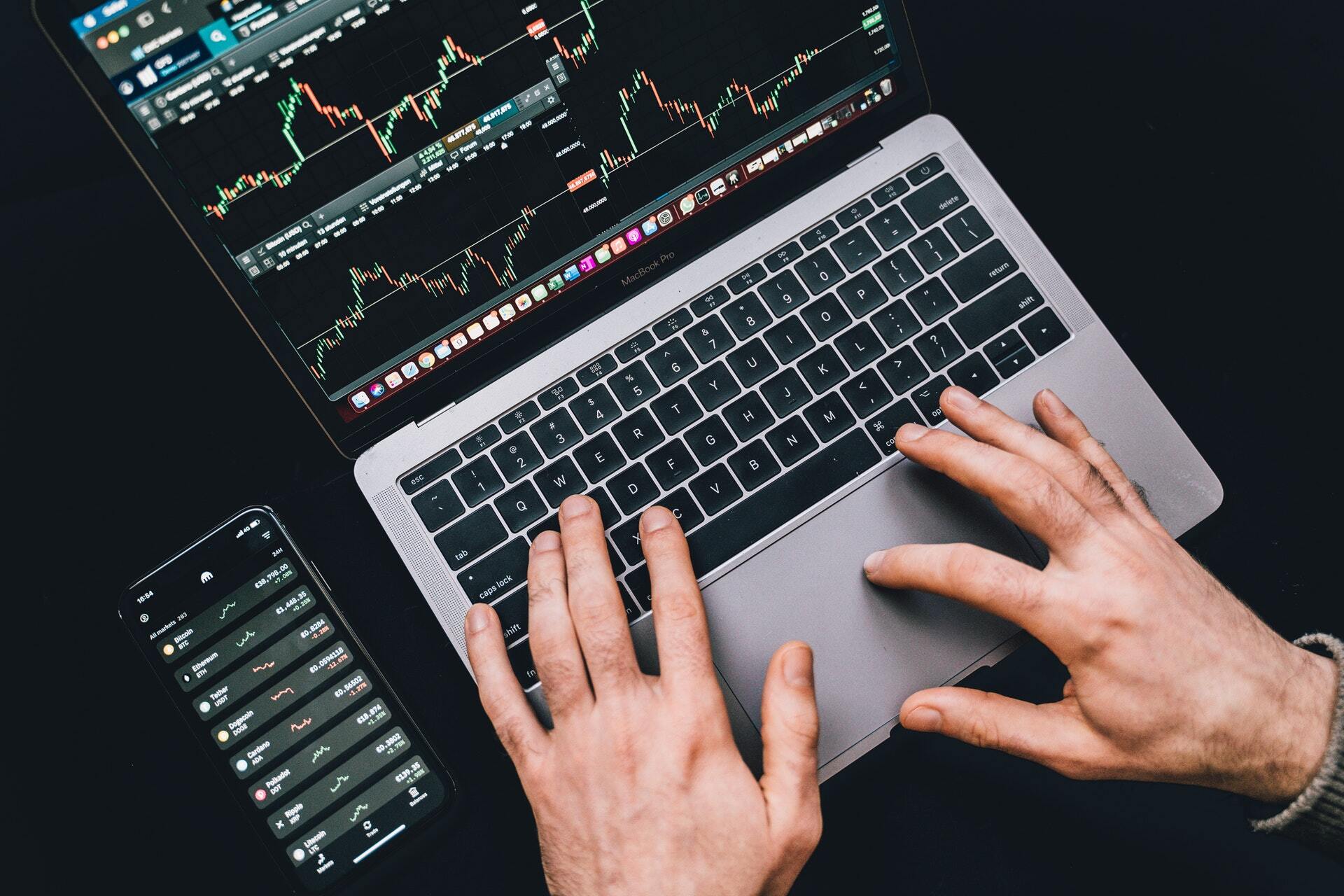 Overhead photo of someone typing on a macbook with a candlestick chart displayed on the screen.