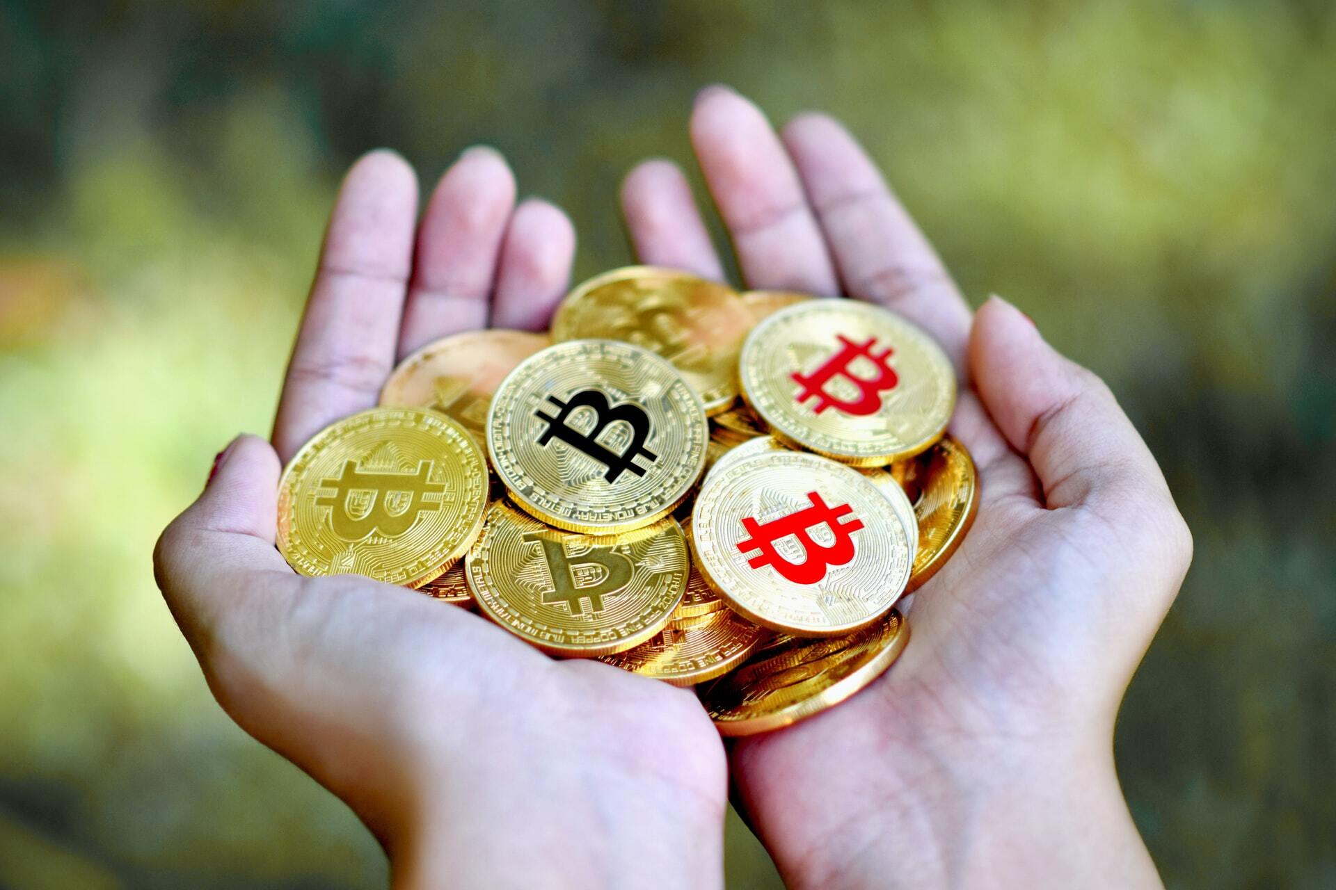 Photo of a pile of bitcoins being held on two hands to illustrate the idea of is bitcoin money.