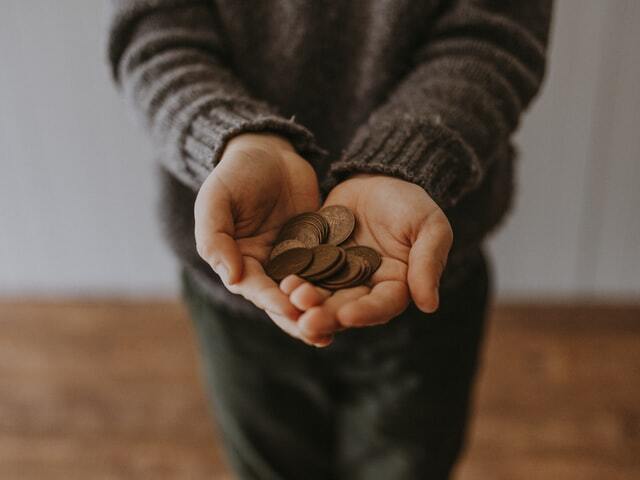 Image of hand extending out holding a pile of coins to depict an act of remittance through stablecoins.