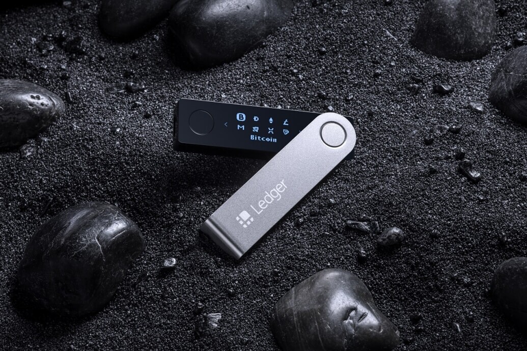 Ledger Nano X placed on the ground backdropped by black sand and stones to illustrate how to set up the ledger nano x