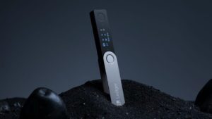 Ledger Nano X vertically placed on a pile of black sand with keylighting from above