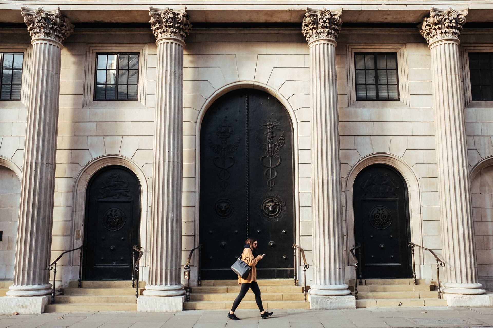 Woman walking in front of a traditional bank, while using a DeFi application.