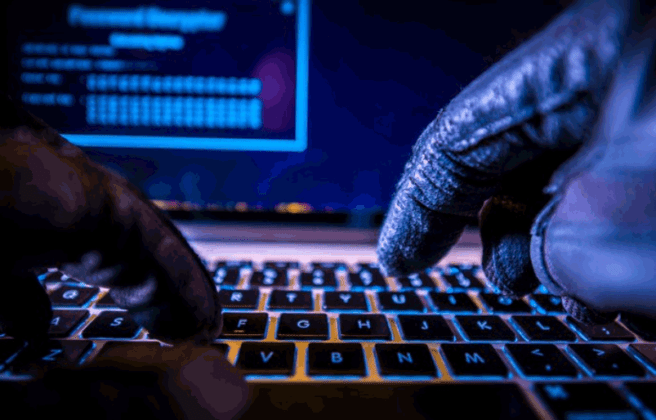 person with leather gloves typing on a glowing keyboard with a monitor behind