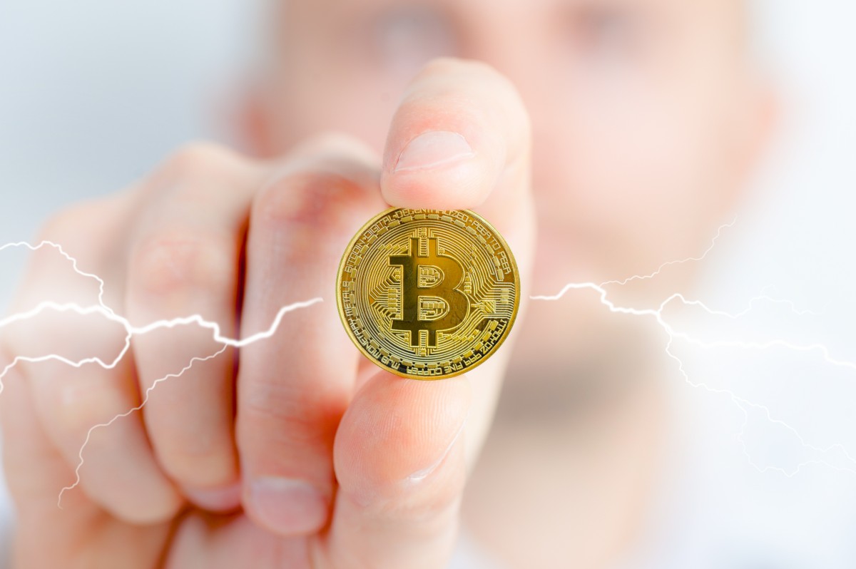 Person holding a physical Bitcoin with electricity coming on either side of the coin.