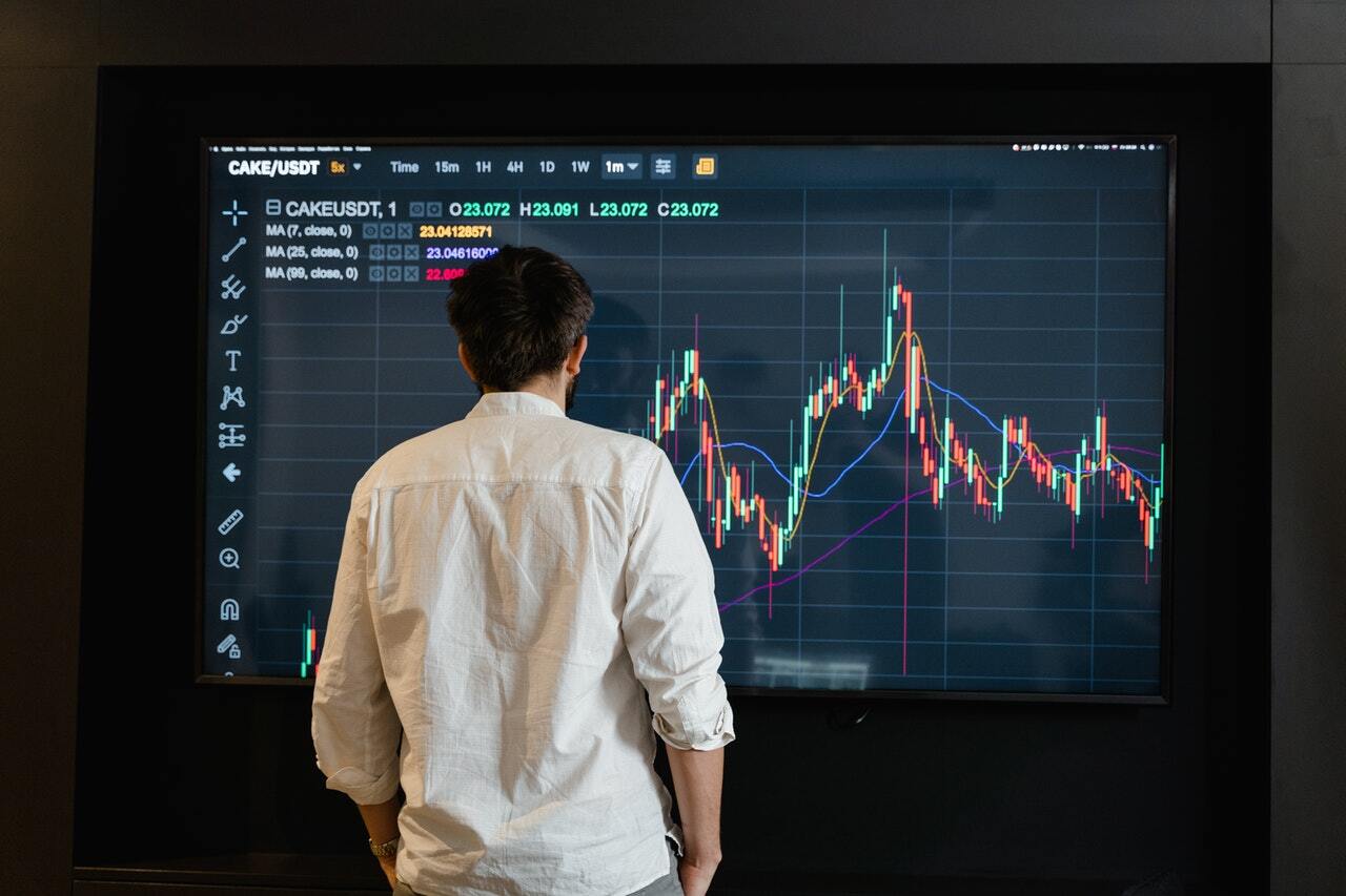 Man standing in front of a large screen showcasing a trading chart.