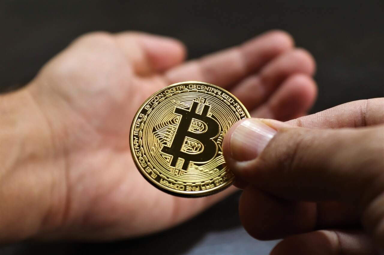 Person holding a golden bitcoin on the tip of the fingers