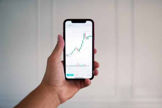 Photo of a hand holding an iphone showing a trading chart on the display.