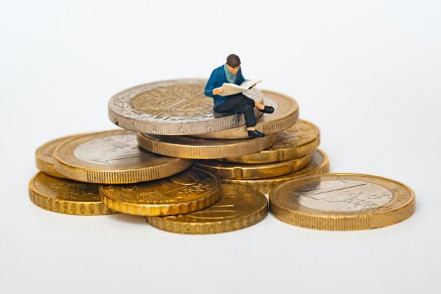 Image of an action figure man sitting on a pile of coins while reading a book to illustrate the topic of best crypto investment techniques in nz