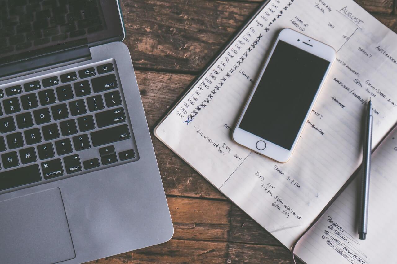 macbook and a notebook on top of a wooden desk