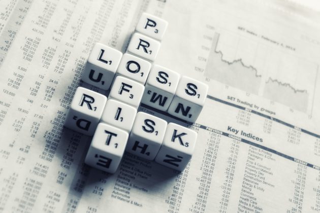 A set of dices that spells out the words profit, loss, and risk arranged on top of a paper.