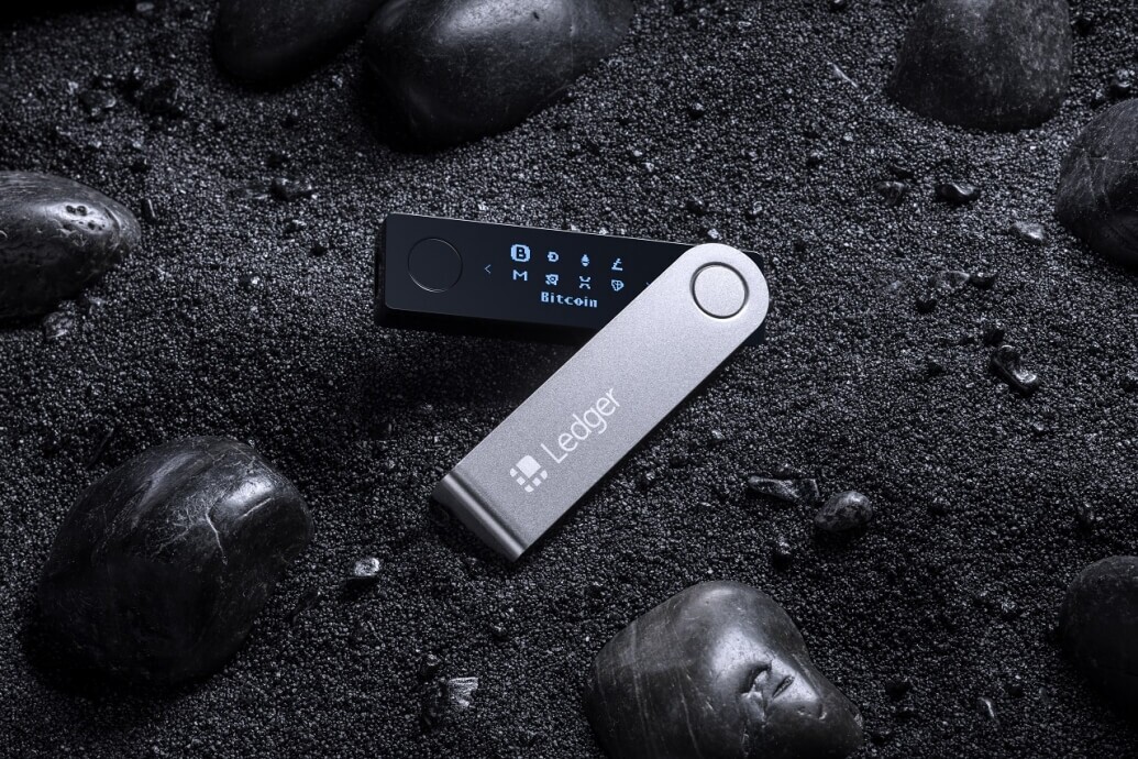 Ledger Nano X placed on the ground backdropped by black sand and stones to illustrate how to set up the ledger nano x Ledger Nano X placed on the ground backdropped by black sand and stones to illustrate how to set up the ledger nano x