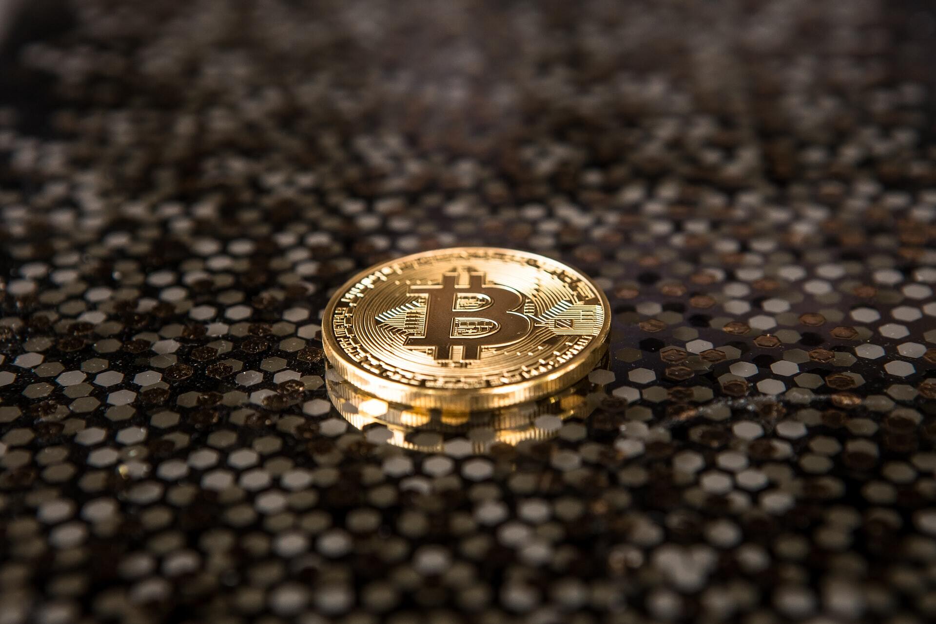 Photo of a physical bitcoin on top of a dark clear table.